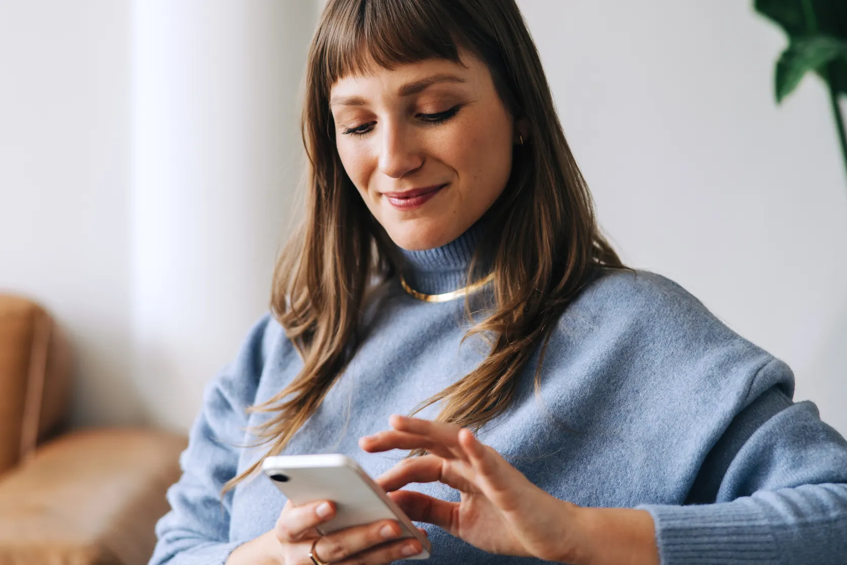A woman in a sweater smiling while looking at her phone.