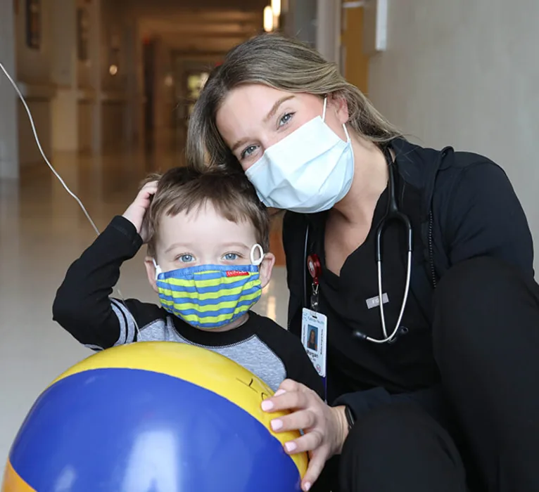 A Kaleida Health nurse crouches beside a young patient holding a beach ball.